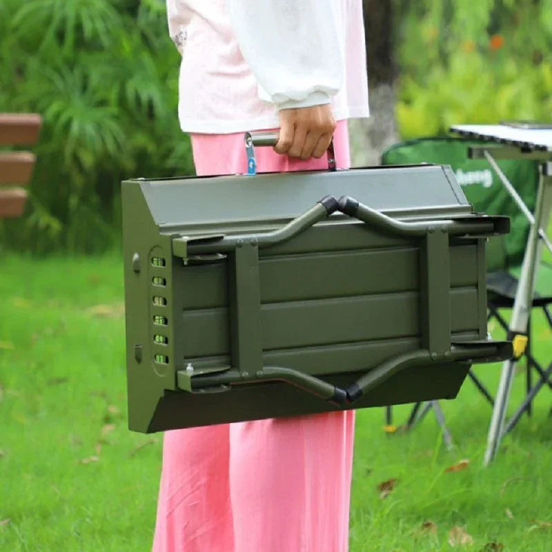 Person in pink pants and white long sleeve blouse holding a green foldable metal table outdoors.