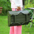 Person in pink pants and white long sleeve blouse holding a green foldable metal table outdoors.