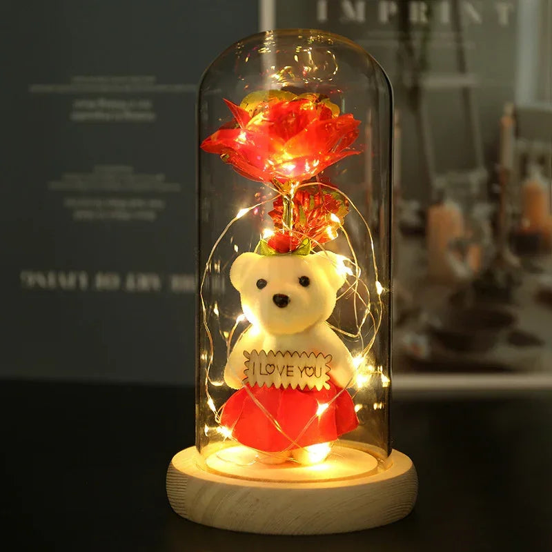 Plush white teddy bear in red skirt with 'I love you' sign under glass dome, fairy lights, and red rose