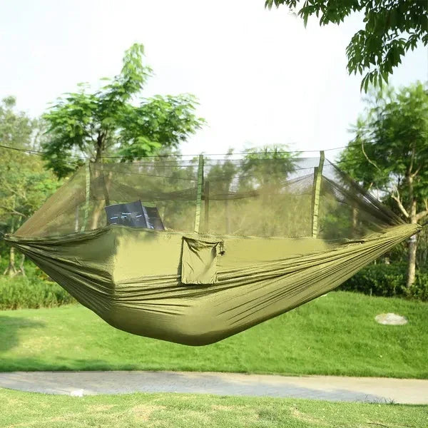 Light green outdoor hammock with attached mosquito net, lightweight nylon material, relaxed fit, hanging between trees in a park.