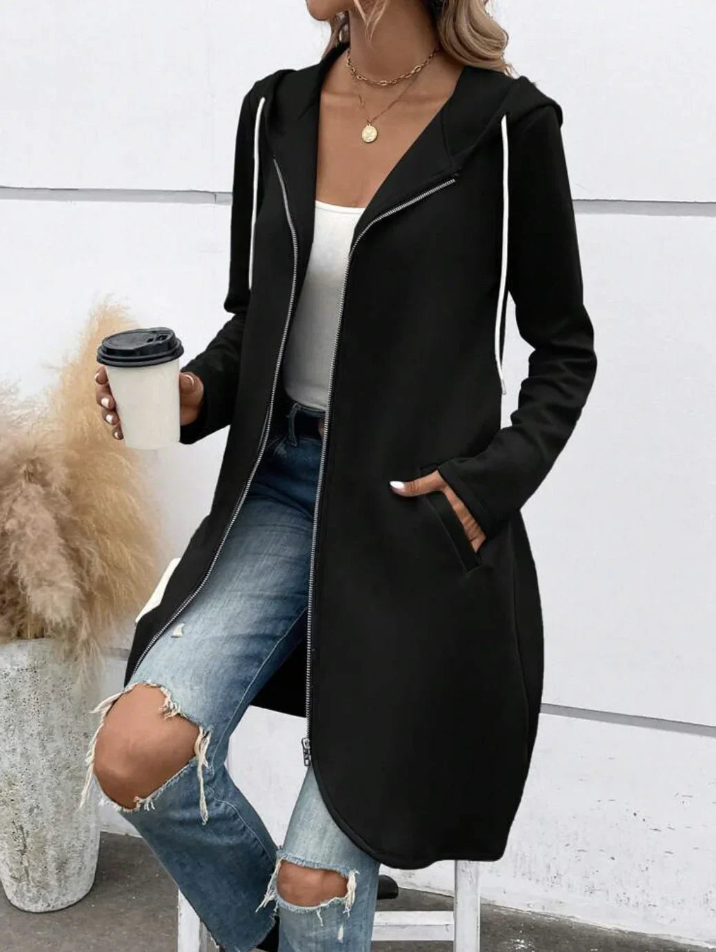 Woman wearing long black zip-up hoodie, white tank top, ripped blue jeans, casual streetwear style