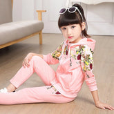 Girl wearing light pink floral hoodie and jogger set, soft cotton, relaxed fit, sitting indoors