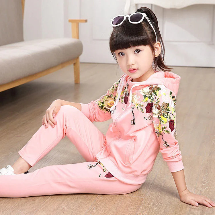 Girl wearing light pink floral hoodie and jogger set, soft cotton, relaxed fit, sitting indoors