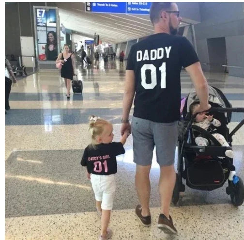 Father and daughter in matching black graphic t-shirts, casual fit, at an airport terminal
