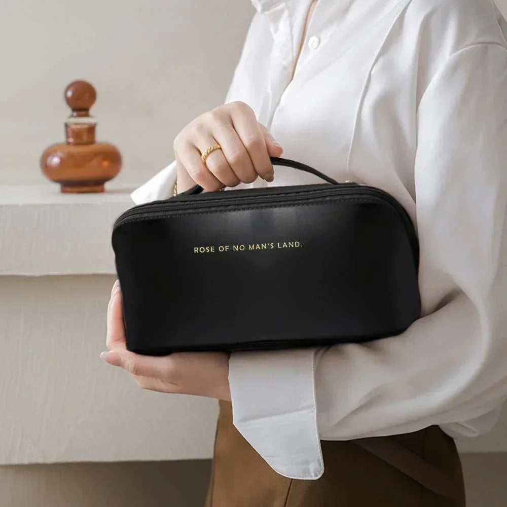 Woman in a white blouse holding a black leather zippered pouch with gold text and top handle
