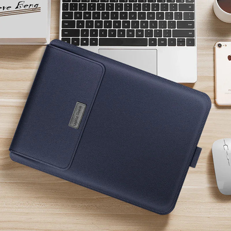 Navy blue leather laptop sleeve with slim fit on wooden desk beside laptop and phone.