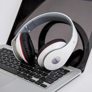 White over-ear headphones with black cushioned ear pads resting on a silver laptop keyboard