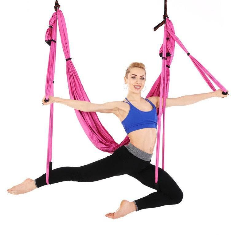 Woman in blue sports bra and black leggings performing aerial yoga in pink hammock