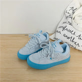 Light blue low-top sneakers with suede finish and bright blue rubber soles on wood surface