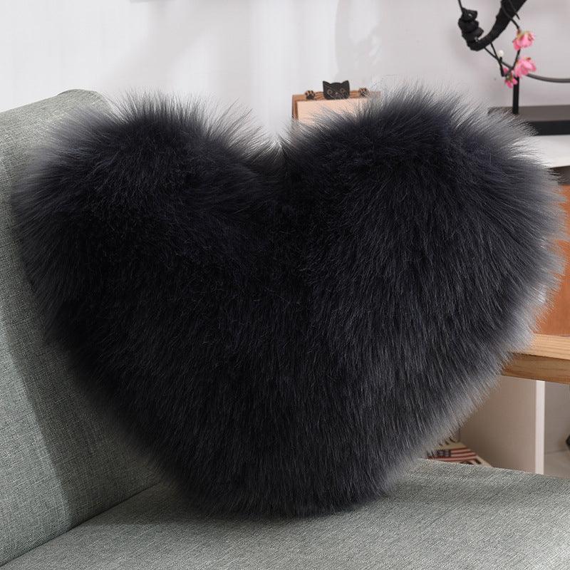 Black heart-shaped faux fur pillow with plush, fluffy texture on a modern sofa