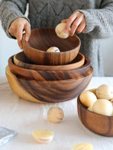 Person in a grey, chunky knit sweater with a loose fit, arranging wooden bowls on a table.