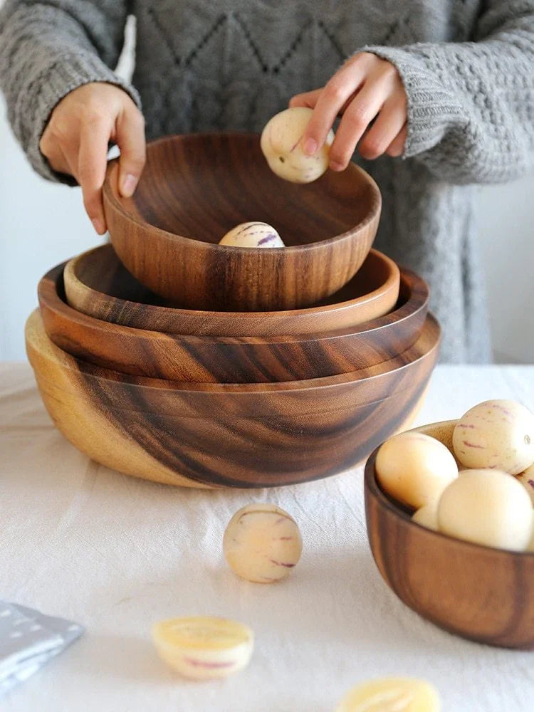 Person in a grey, chunky knit sweater with a loose fit, arranging wooden bowls on a table.