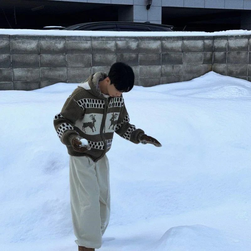 Person in a chunky knit zip-up sweater with deer pattern, loose cream pants, and mittens standing in snow.