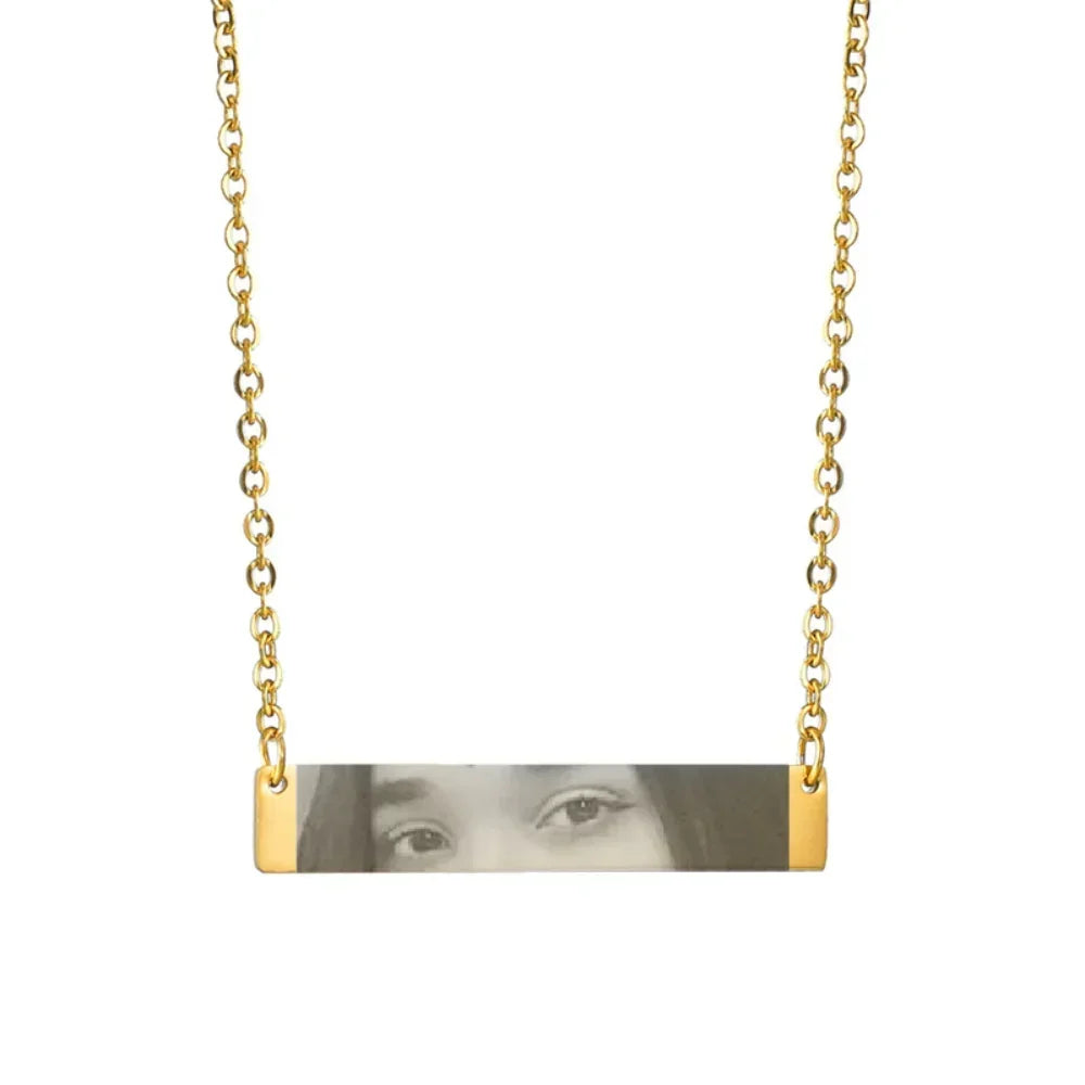 Gold chain necklace with horizontal bar pendant featuring engraved face details, minimalist style