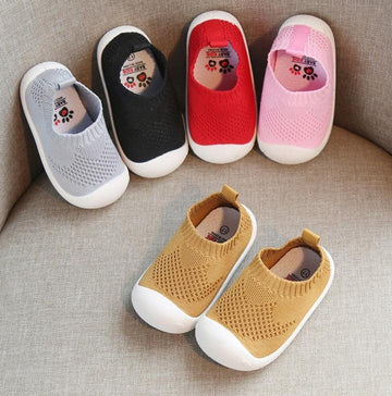 Colorful knit slip-on baby shoes with rubber soles, displayed on a sofa.