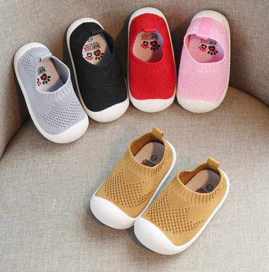 Colorful knit slip-on baby shoes with rubber soles, displayed on a sofa.