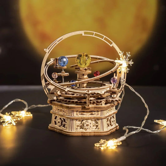 Wooden mechanical orrery model with colorful planets, surrounded by string lights