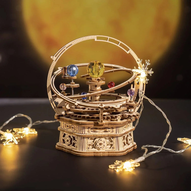 Wooden mechanical orrery model with colorful planets, surrounded by string lights