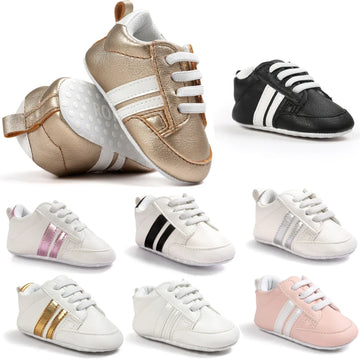 Assorted baby sneakers in metallic gold, black, white, and pink with faux leather material and sporty striped design.