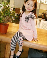 Girl wearing a pink long-sleeve tunic with striped black and white leggings and bow detail.