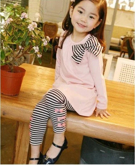 Girl wearing a pink long-sleeve tunic with striped black and white leggings and bow detail.