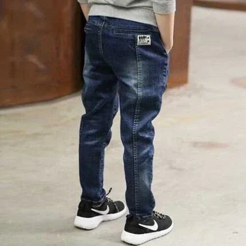 Child wearing dark blue denim jeans with tapered fit and casual sneakers, standing indoors