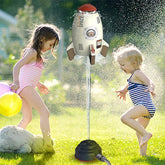 Children in striped and pink swimsuits playing with a rocket-shaped outdoor water sprinkler