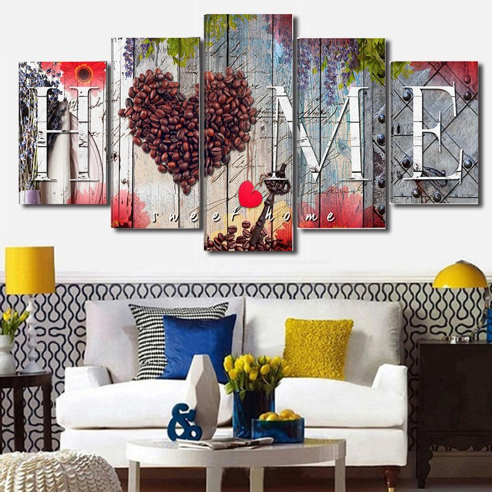 Modern living room with a white sofa, bold patterned pillows, yellow and blue accents, and a colorful wall art panel spelling HOME with coffee beans forming a heart.
