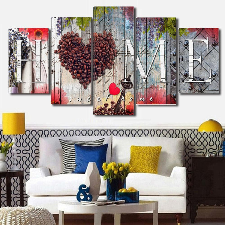 Modern living room with a white sofa, bold patterned pillows, yellow and blue accents, and a colorful wall art panel spelling HOME with coffee beans forming a heart.