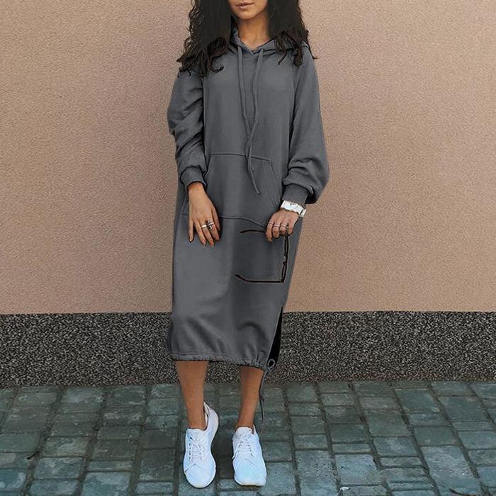 Woman wearing a loose-fit gray hoodie dress with long sleeves and drawstring hood, styled with white sneakers.