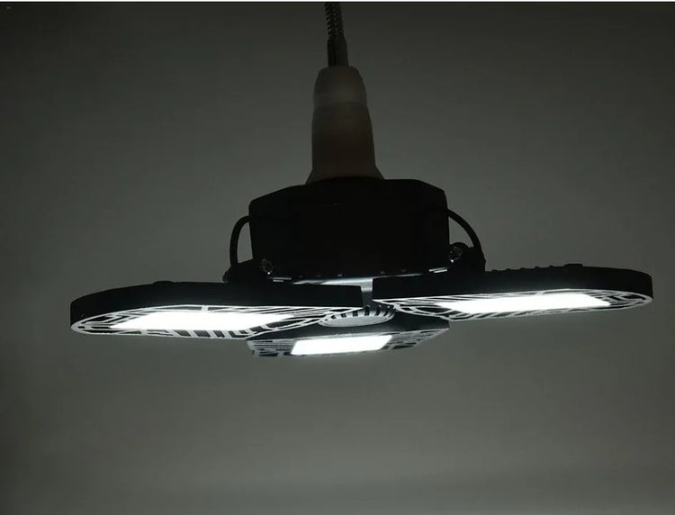 Modern LED ceiling light fixture with three adjustable black panels, emitting bright white light.