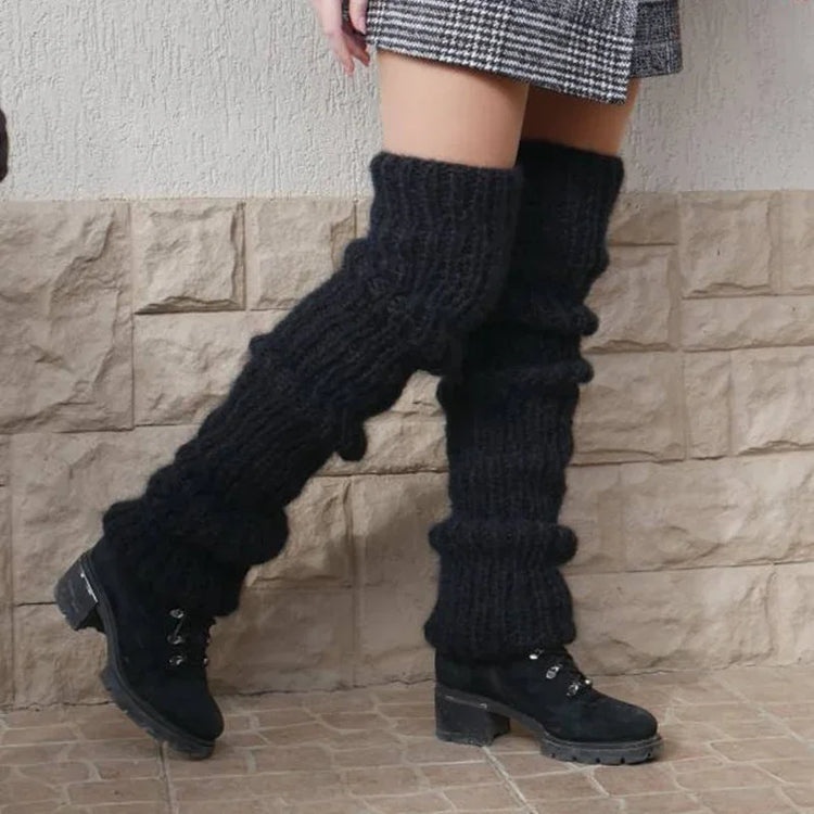 Chunky black knit leg warmers with ribbed texture, paired with black boots and plaid mini skirt