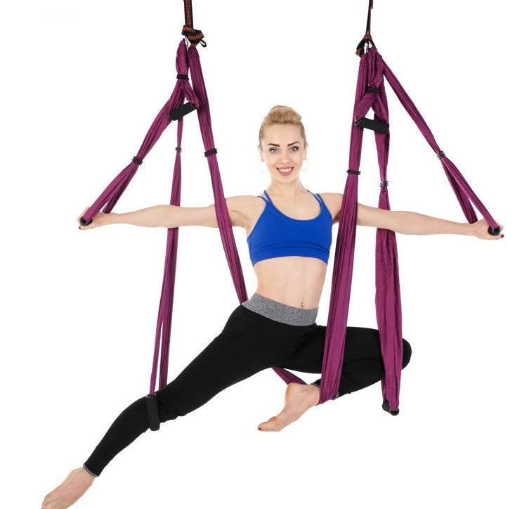 Woman in blue sports bra and black leggings performing aerial yoga with purple hammock, fitted athletic wear