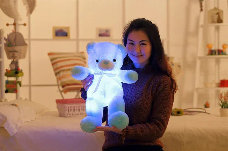 Woman in a brown knit sweater holding a glowing blue plush teddy bear indoors