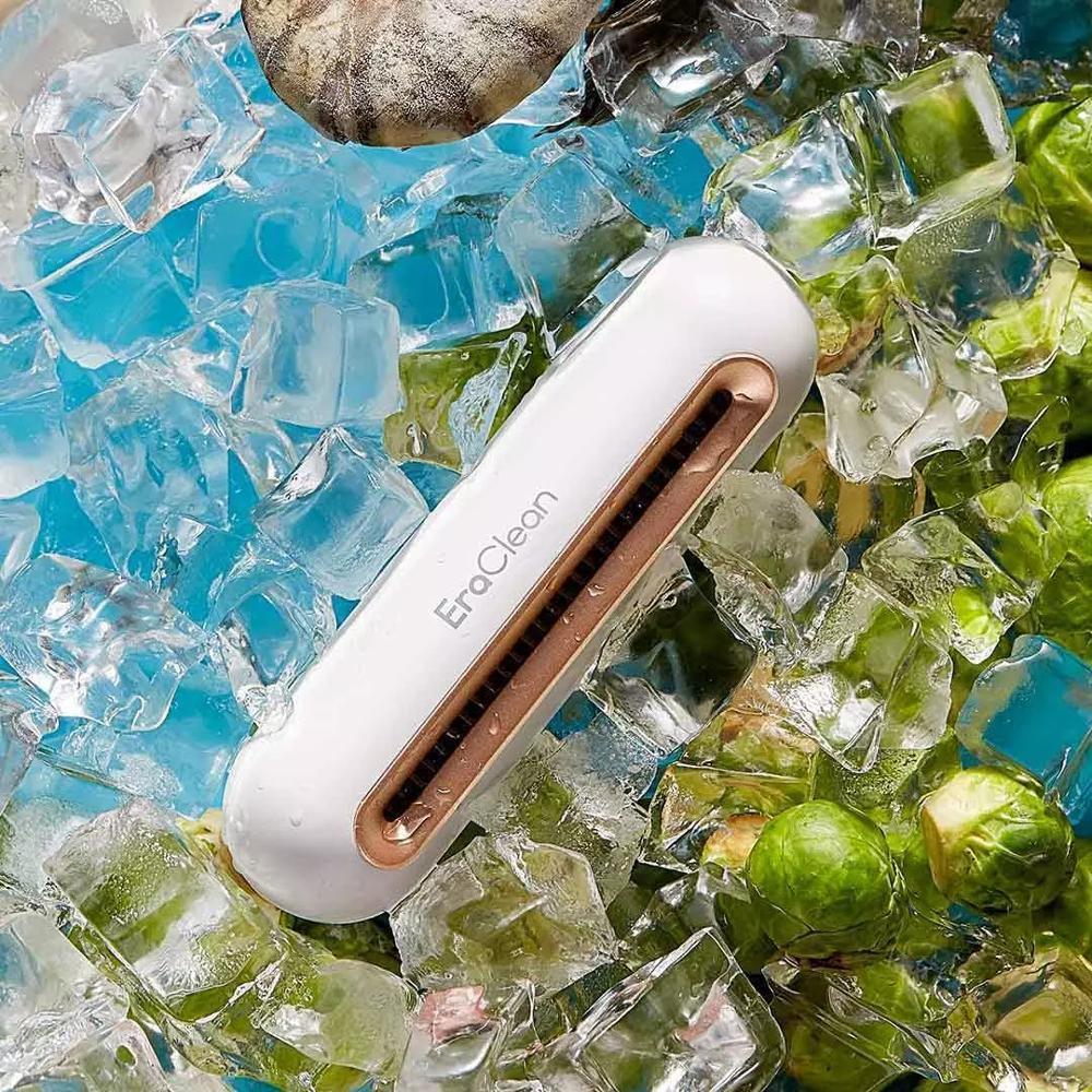 White handheld electric cleaning brush with gold accent on ice and vegetables