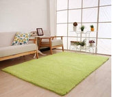 Modern living room with light green plush area rug, light wood flooring, neutral sofa and armchair.