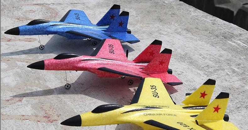 Three foam SU-35 model jets in blue, red, and yellow with black accents on concrete.