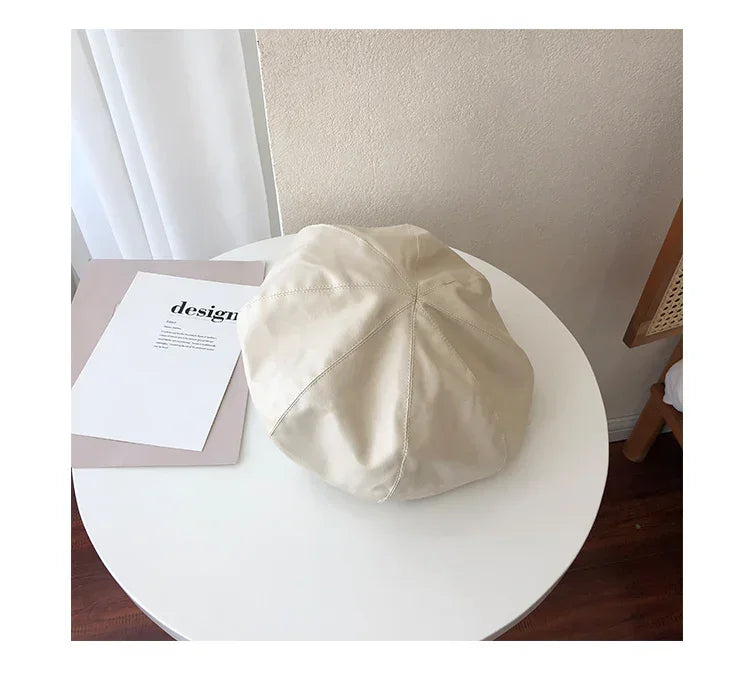 Beige faux leather beret hat with relaxed fit on a white table, modern minimalist style.