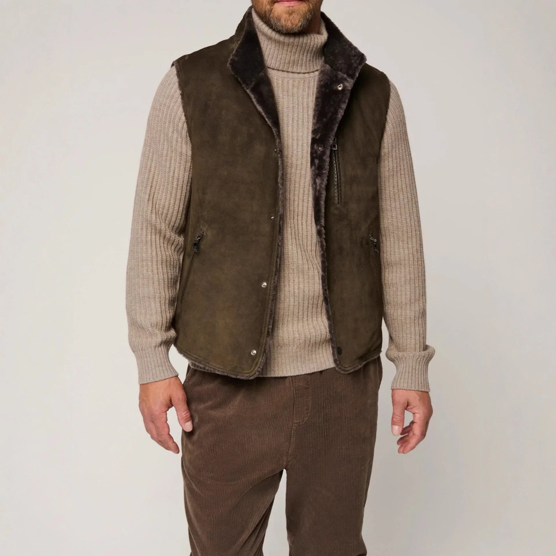Man wearing a brown suede shearling vest over a beige ribbed turtleneck sweater and brown corduroy pants