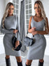 Woman wearing fitted gray ribbed knit dress, long sleeves on left, sleeveless on right, knee-high black boots and black handbag, modern indoor setting.