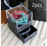 Gift box with artificial rose flower on top and drawer displaying blue beaded bracelets