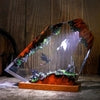 Glowing fantasy diorama with dragons, castle, and mossy terrain in resin art piece on wooden base