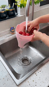 Pink plastic colander with ergonomic handle rinsing red apples under kitchen faucet