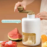 Manual white and gold ice crusher with hand crank, surrounded by fresh fruit on a kitchen table
