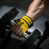 Man wearing yellow and black fitted workout gloves lifting a black dumbbell in gym.