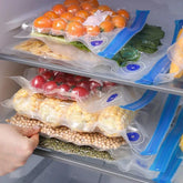 Assorted fruits and vegetables in clear reusable vacuum sealer bags inside a refrigerator.
