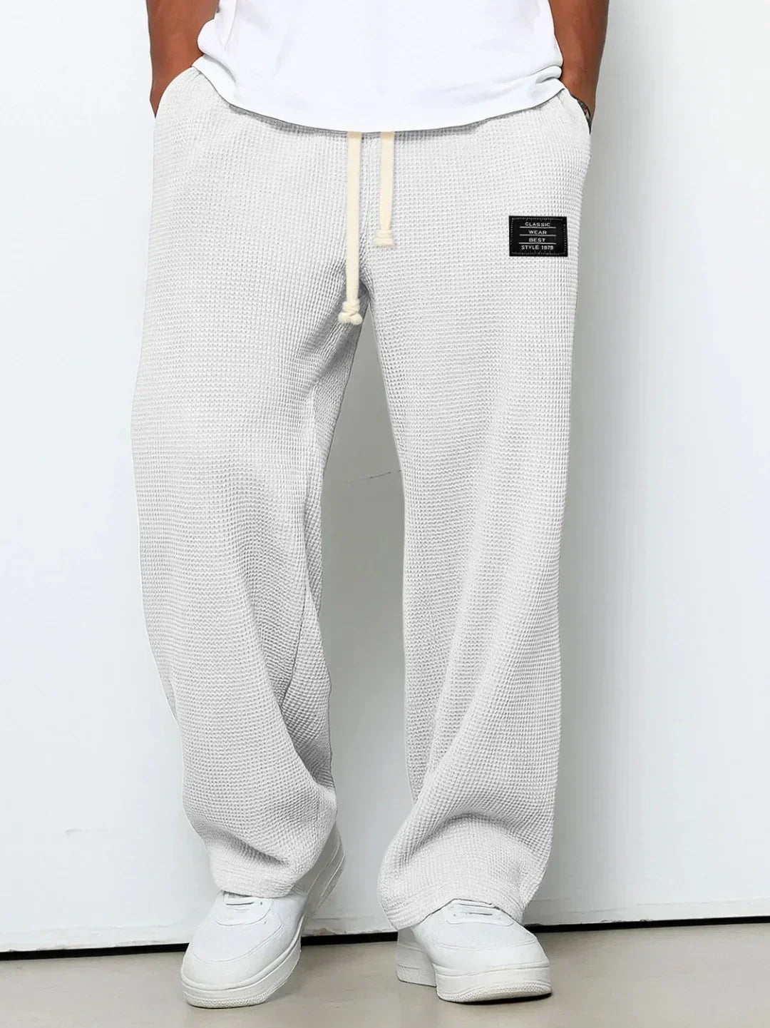 White waffle knit drawstring pants with relaxed fit and side patch, styled with white sneakers.