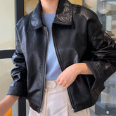 Black faux leather jacket with zipper, relaxed fit, styled with light blue top and white pants