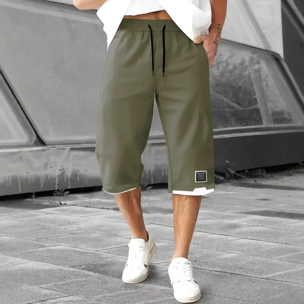 Man wearing olive green knee-length drawstring shorts with relaxed fit and white trim, casual streetwear style.