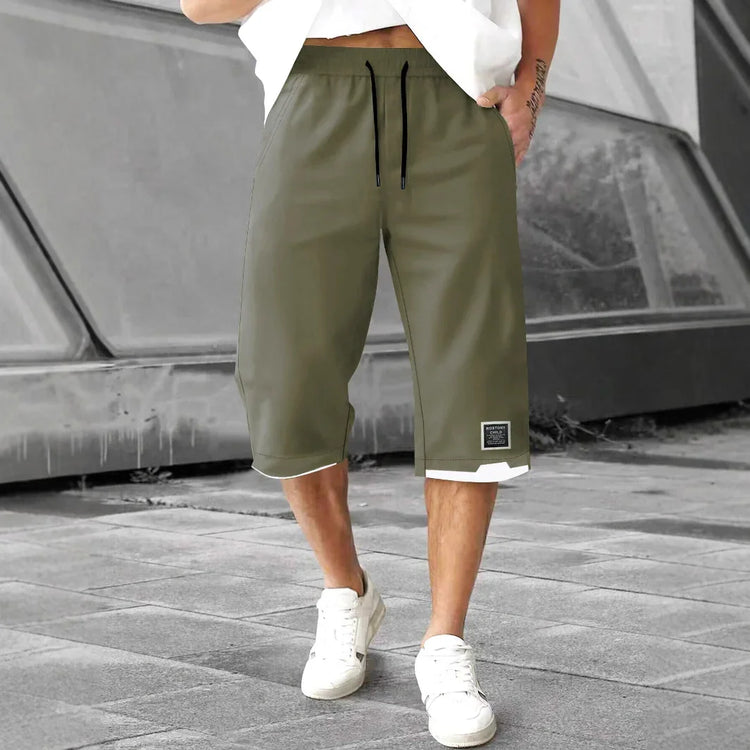 Man wearing olive green knee-length drawstring shorts with relaxed fit and white trim, casual streetwear style.